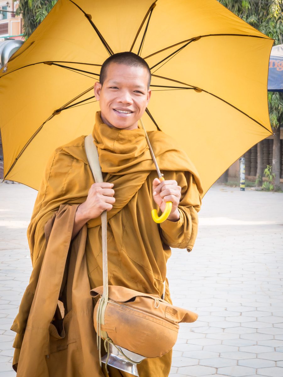 Young monk in yellow-orange robes with matching umbrella and alms bowl