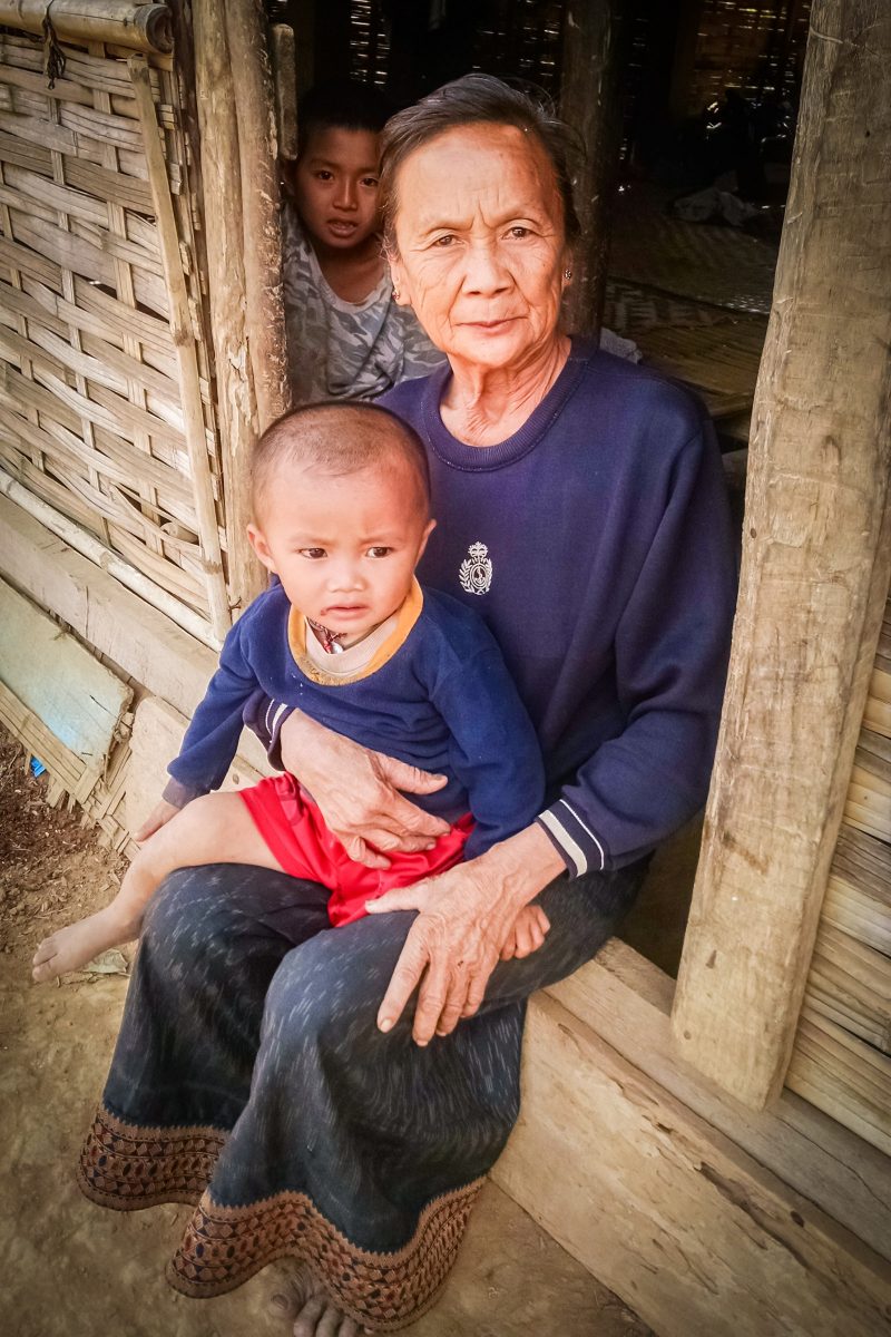 Old woman holds small child on doorstep of wooden house