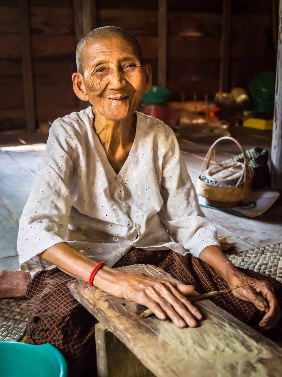Very old smiling woman rolling incense sticks on wood plank