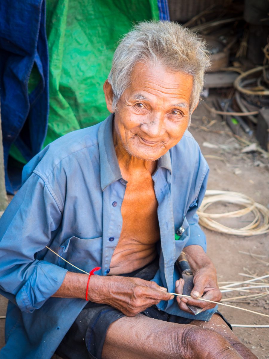 Cambodian man seated on ground weaving reed baskets
