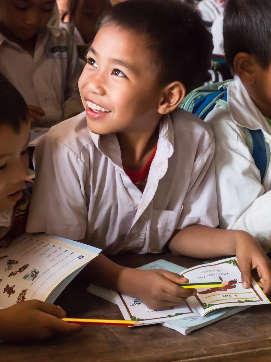 Young boy in school smiles while holding a book and pencil