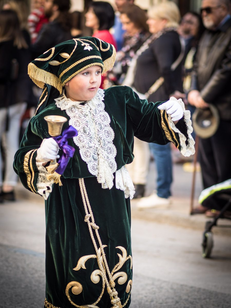 Young boy dressed in antique green velvet and gold costume walks and rings handbell