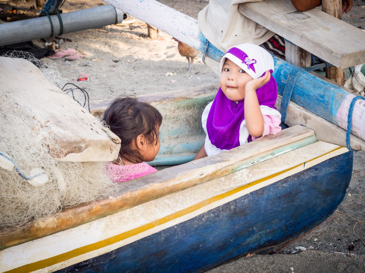 Two girls in a blue canoe with fishing net, one with purple and white headscarf