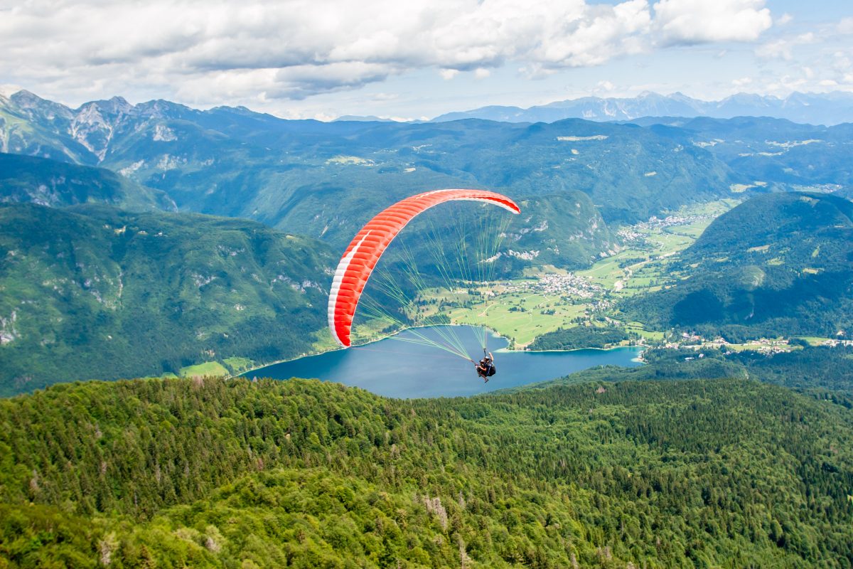 Paraglider with red canopy flies over green mountains and lake