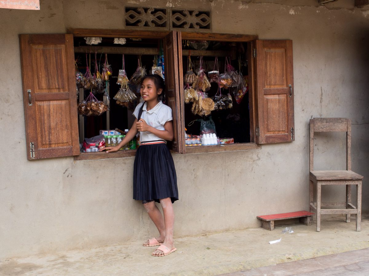 Girl in school uniform stands at shop window with hanging bags of snacks
