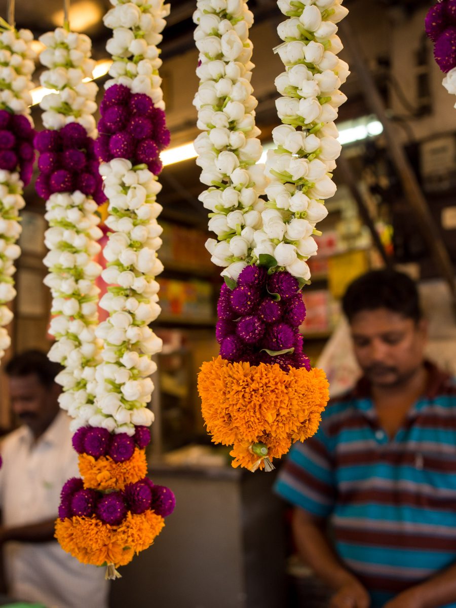 White, pink, and orange flower offering necklaces, blurred men in background