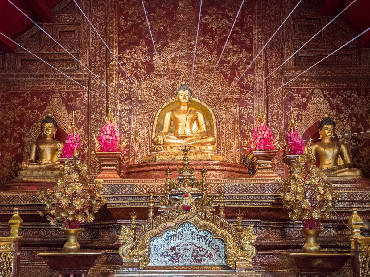 Three gold Buddhas on red and gold alter in front of red wall with gold patterns