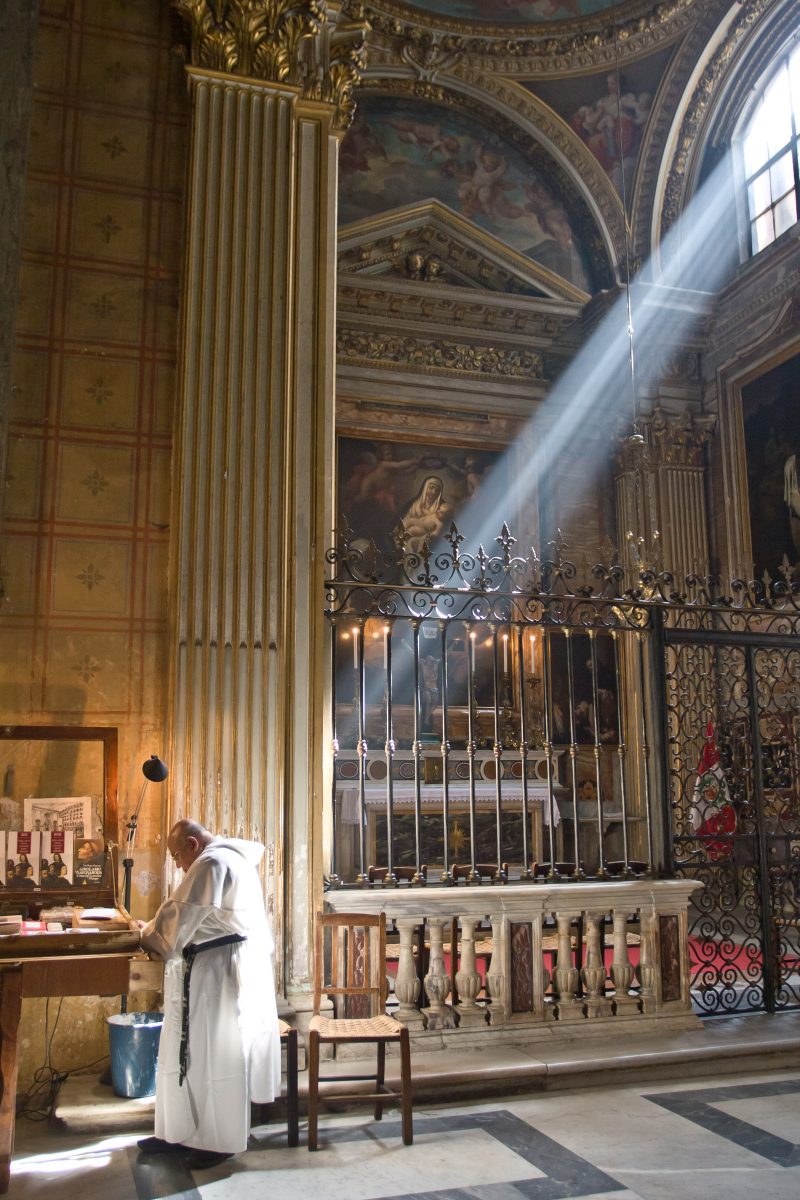 Light streams in church window onto priest in white robe in front of alter