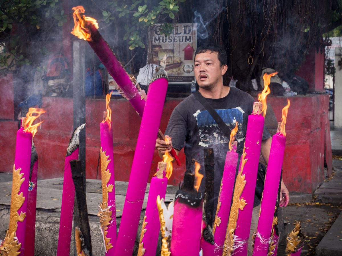 Man lights huge pink and gold incense sticks on sidewalk