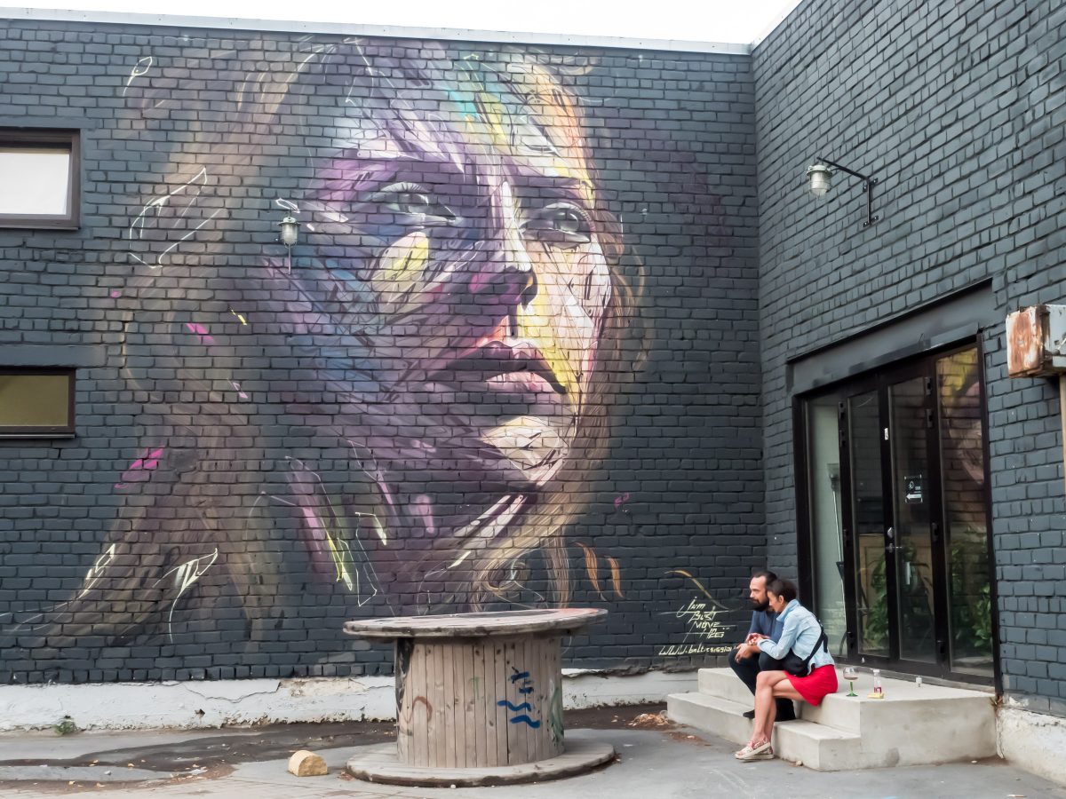 Couple sitting in front of mural of woman's face on black brick wall