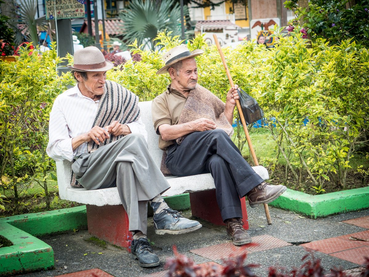 Two old men in hats sit on bench in plaza